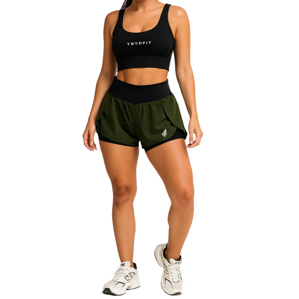Mulher vestindo conjunto fitness preto e verde, top esportivo e shorts, ideal para treino.