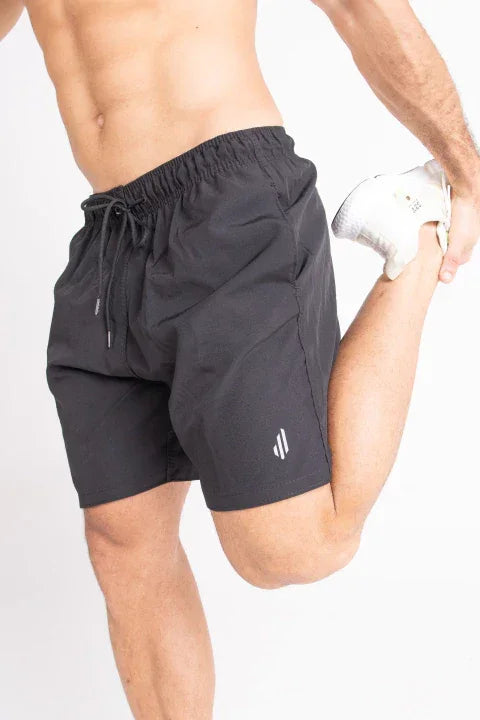 Homem vestindo shorts esportivo preto para treino, alongando a perna, moda fitness masculina